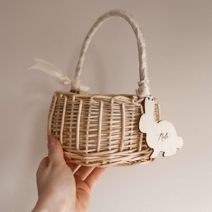 Personalisiertes Osterkörbchen aus geflochtenem Holz mit Henkel und Hasenanhänger aus Holz mit graviertem Namen, in der Hand gehalten vor neutralem Hintergrund.