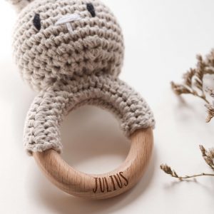Gehäkelte Babyrassel in Form eines Hasen an einem Holzring mit Namensgravur in einem neutralen Setting