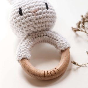 Gehäkelte Babyrassel in Form eines Hasen an einem Holzring mit Namensgravur in einem neutralen Setting