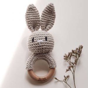 Gehäkelte Babyrassel in Form eines Hasen an einem Holzring mit Namensgravur in einem neutralen Setting