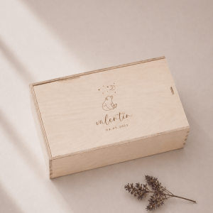 Minimalistische Aufnahme einer personalisierten Holz-Erinnerungskiste mit Gravur „Valentin“ und Datum, auf hellem Hintergrund mit sanftem Sonnenlicht und einem kleinen getrockneten Zweig im Vordergrund.