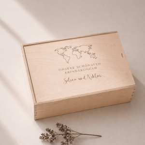 Minimalistische Aufnahme einer personalisierten Holz-Erinnerungskiste mit Gravur „Unsere schönsten Erinnerungen Selina und Niklas" und einer Weltkarte, auf hellem Hintergrund mit sanftem Sonnenlicht und einem kleinen getrockneten Zweig im Vordergrund.