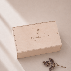 Minimalistische Aufnahme einer personalisierten Holz-Erinnerungskiste mit Gravur „Isabella“ und Datum, auf hellem Hintergrund mit sanftem Sonnenlicht und einem kleinen getrockneten Zweig im Vordergrund.