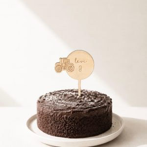 Großer Cake Topper aus Lindenholz mit Traktor-Motiv, dem Namen Levi und der Zahl 8 in einem Schokokuchen in minimalistischem Hintergrund mit natürlichem Sonnenlicht
