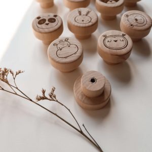 12 Helle runde Möbelknöpfe aus Holt mit verschiedenen Tiermotiven in einem minimalistischen Hintergrund mit natürlichem Sonnenlicht. Die Möbelknöpfe eignen sich perfekt für die Ikea Hemnes Kommode