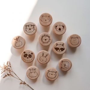 12 Helle runde Möbelknöpfe aus Holt mit verschiedenen Tiermotiven in einem minimalistischen Hintergrund mit natürlichem Sonnenlicht. Die Möbelknöpfe eignen sich perfekt für die Ikea Hemnes Kommode