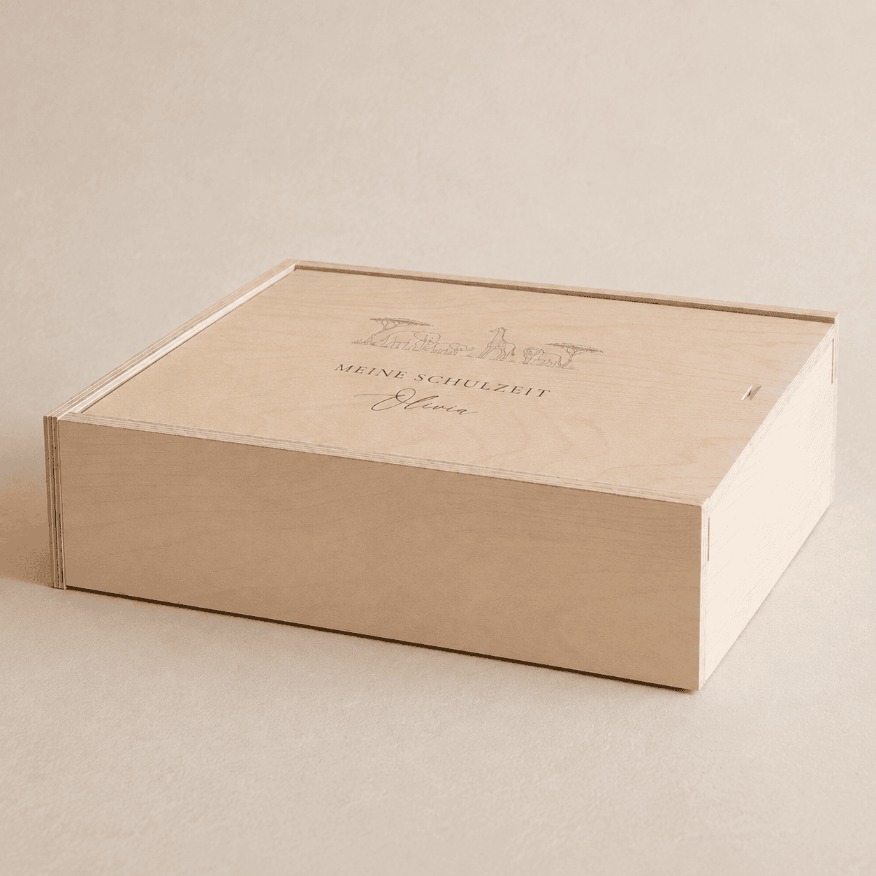 Personalisierte Erinnerungsbox aus hellem Holz mit dem eingravierten Text "Meine Schulzeit" und Safaritiere als Design auf einem minimalistischen, cremefarbenen Hintergrund mit weichem Tageslicht.