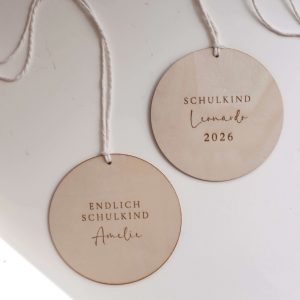 zwei runde Holzscheiben mit weißer Kordel und den Texten "Endlich Schulkind Amelie" und "Schulkind Leonardo 20262" in minimalistischem Hintergrund