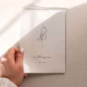 personalisierte mutterpasshülle mit schlichtem design eines Babys ala fine line zeichnung dem text "mutterpass alina" von einer hand gehalten in minimalistischem hintergrund mit natürlichem sonnenlicht