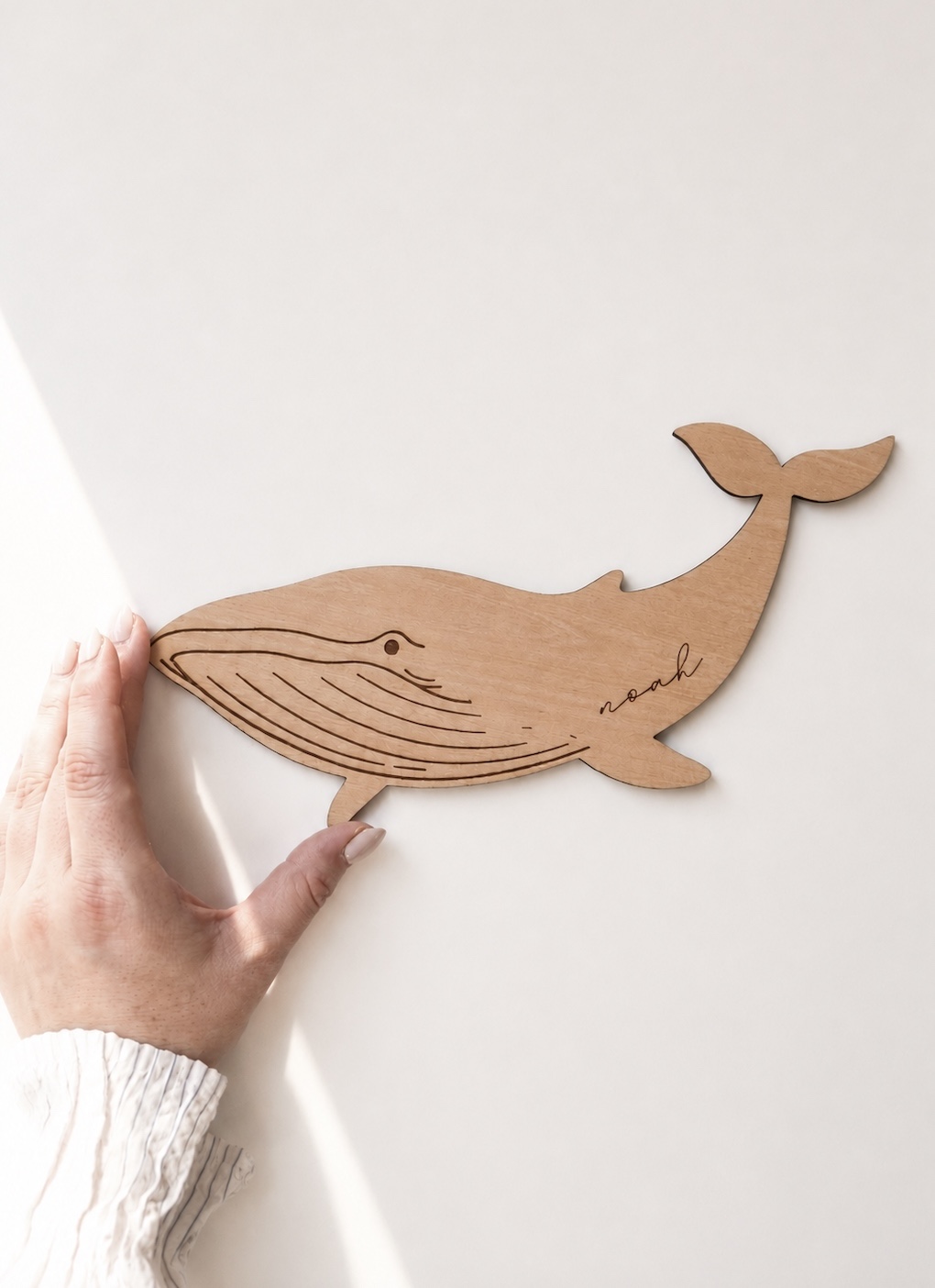 Schild aus hellem Holz in Form eines Wals mit dem Namen Noah eingraviert in minimalistischem Hintergrund