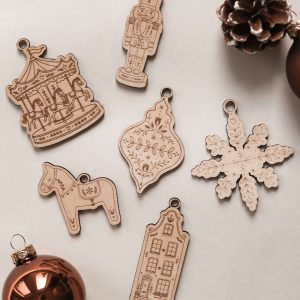 Christbaumschmuck aus Holz im Scandi-Stil, 6 verschiedene weihnachtliche Motive mit filigraner Lasergravur, dekoriert mit Weihnachtskugeln und Tannenzapfen.