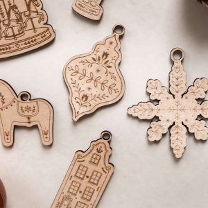 Christbaumschmuck aus Holz im Scandi-Stil, 6 verschiedene weihnachtliche Motive mit filigraner Lasergravur, dekoriert mit Weihnachtskugeln und Tannenzapfen.